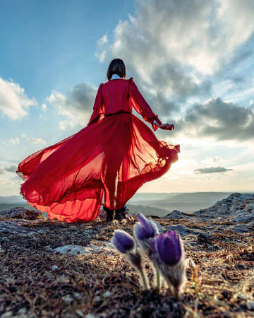 Rise of the mystic. sunset over the clouds with a girl in a long red dress. There is a dream grass in the meadow with purple flowers.の写真素材