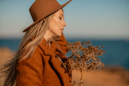 A woman walking along the coast near the sea. An elegant lady in a brown coat and a hat with fashionable makeup walks on the seashoreの写真素材
