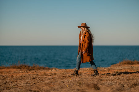 A woman walking along the coast near the sea. An elegant lady in a brown coat and a hat with fashionable makeup walks on the seashoreの写真素材