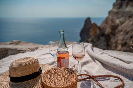 A picnic blanket, champagne, two glasses, a hat and a straw purse. Top on the mountain against the background of the sea and rocks in the sea.の写真素材