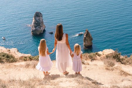 Mom holds the hands of two daughters. They in white dresses stand with their backs to the spectators...