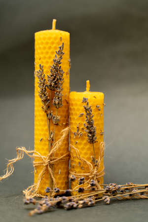 Two beeswax candles on a gray background. The candles are decorated with sprigs of lavender and tied with a jute rope.の写真素材