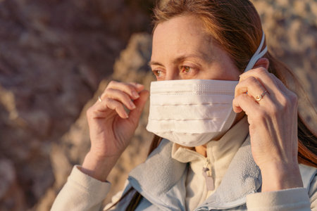 Masked redhead girl dressed in bright clothes outdoors on a sunny day. pandemic