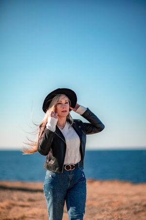 A blonde in a stylish black leather jacket walks along the seashore.