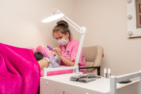 Master lashmaker, diligently extends eyelashes to the client, on the couch, in the beauty salon. A...