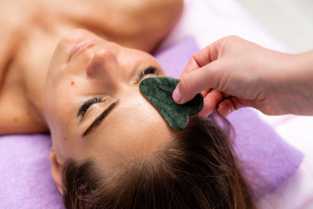 Relaxing massage. European woman getting quartz guache face massage in spa salon, side view