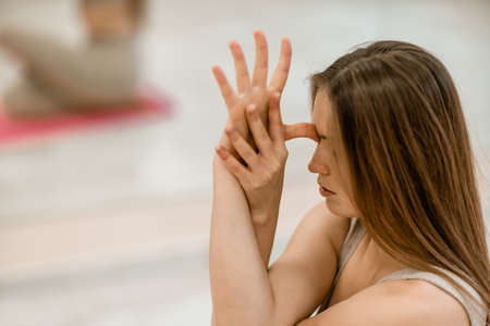 Young woman doing yoga in the gym. A girl with long hair and in a beige tracksuit stands in a cow pose on a pink carpet. A woman performs Gomukhasana.の写真素材