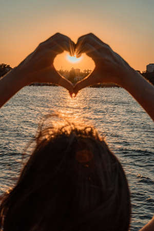 Silhouette against the sunset - hands folded in the shape of a heart. Sun with rays between the palms. Concept for Valentines Day, declaration of love. Minimalism, space for text, warm colors.の写真素材