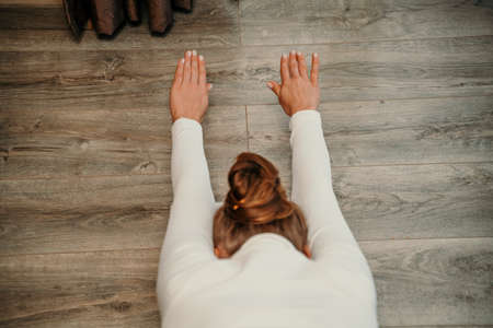 Adult athletic woman, in white bodysuit, performing fascia exercises on the floor - caucasian woman using a massage foam roller - a tool to relieve tension in the back and relieve muscle pain - the concept of physiotherapy and stretching training.の写真素材