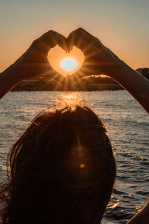 Silhouette against the sunset - hands folded in the shape of a heart. Sun with rays between the palms. Concept for Valentines Day, declaration of love. Minimalism, space for text, warm colors.の写真素材