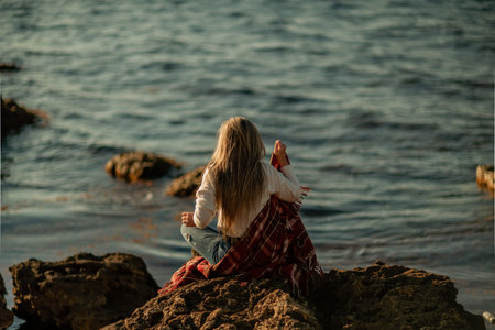 Attractive blonde Caucasian woman enjoying time on the beach at sunset, sitting in a blanket and...