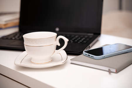 White desktop with laptop, coffee mug, phone and notebook for remote work or study. Office computer workplace in home interiorの写真素材