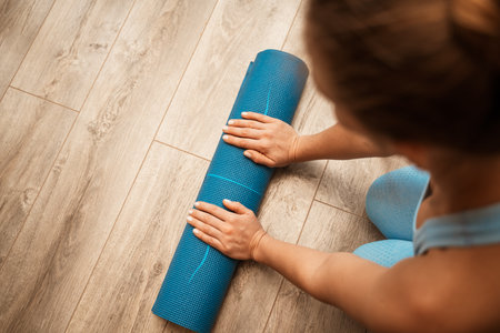 Woman hands rolled up yoga mat on gym floor in yoga fitness training room. Home workout woman close up hands rolling foam yoga gym mat. Woman barefoot home workout sportive healthy lifestyle conceptの写真素材