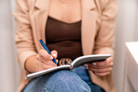 European woman writes in a notebook. She is wearing a beige jacket and jeans.の写真素材