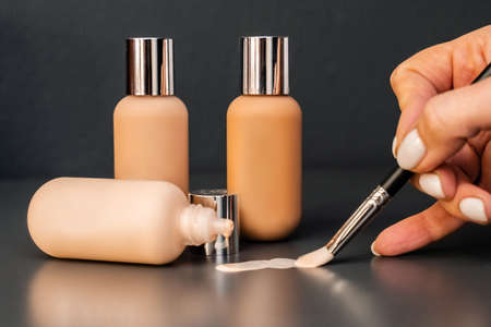 Foundation for the face in glass jars of dark and light shades. Professional makeup for makeup artists. A womans hand holds a brush and smears foundation.の写真素材