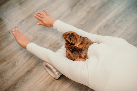 Adult athletic woman, in white bodysuit, performing fascia exercises on the floor - caucasian woman using a massage foam roller - a tool to relieve tension in the back and relieve muscle pain - the concept of physiotherapy and stretching training.の写真素材