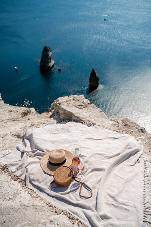 A picnic blanket, champagne, two glasses, a hat and a straw purse. Top on the mountain against the background of the sea and rocks in the sea.の写真素材
