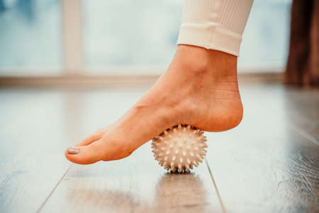 Athletic slim caucasian woman doing thigh self-massage with a massage ball indoors. Self-isolating massageの写真素材