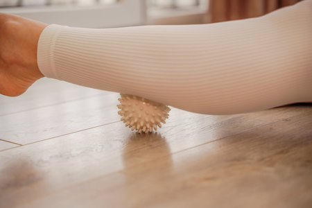 Athletic slim caucasian woman doing thigh self-massage with a massage ball indoors. Self-isolating...