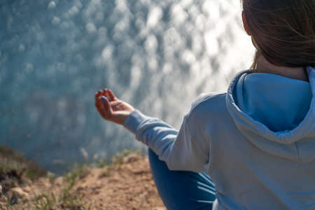 Woman tourist enjoying the sunset over the sea mountain landscape. Sits outdoors on a rock above the sea. She is wearing jeans and a blue hoodie. Healthy lifestyle, harmony and meditationの写真素材