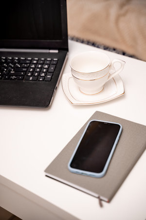 White desktop with laptop, coffee mug, phone and notebook for remote work or study. Office computer...