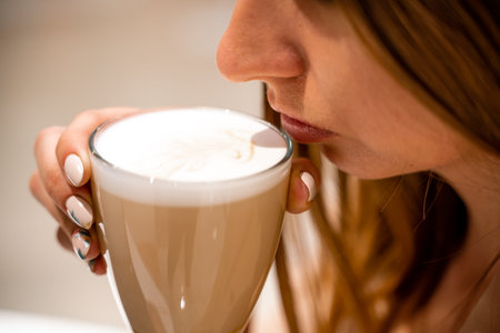 Close-up of beautiful female hands holding a large white cup of cappuccino. A woman is sitting in a...