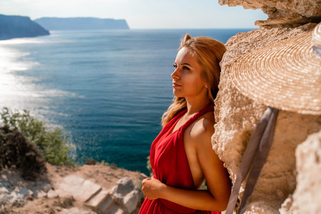 Smiling young woman in a red dress looks at the camera. A beautiful tanned girl enjoys her summer holidays at the sea. Portrait of a stylish carefree woman laughing at the ocean.の写真素材