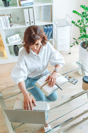 Woman in the office at the computer. She is dressed in a white shirt and blue jeans sitting at a...