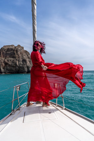 Attractive middle-aged woman in a red dress on a yacht on a summer day. Luxury summer adventure, outdoor activities.の写真素材