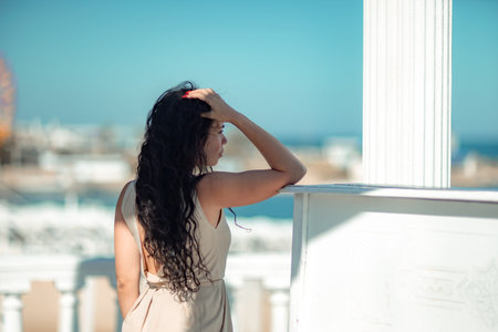 Sea woman rest. A woman with long curly hair in a beige dress stands with her back and looks at the...