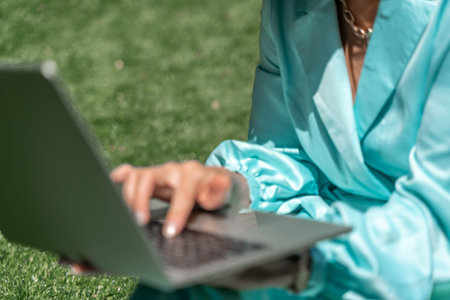 a young beautiful woman with blond curly hair in glasses and a blue dress sits on the grass in...