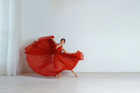 Dancer in a red flying dress. Woman ballerina dancing on a white studio backgroundの写真素材