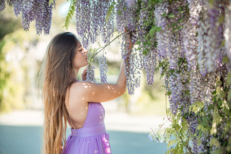 Woman wisteria lilac dress. Thoughtful happy mature woman in purple dress surrounded by chinese wisteriaの写真素材