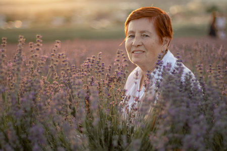 A middle-aged woman sits in a lavender field and enjoys aromatherapy. Aromatherapy concept, lavender oil, photo session in lavenderの写真素材