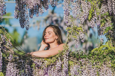 Woman wisteria lilac dress. Thoughtful happy mature woman in purple dress surrounded by chinese wisteriaの写真素材