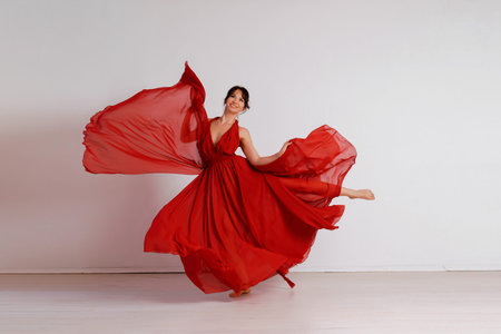 Dancer in a red flying dress. Woman ballerina dancing on a white studio backgroundの写真素材