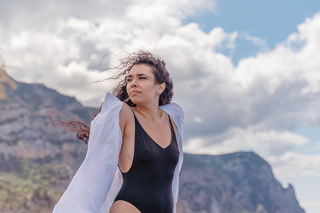 Woman on a yacht. Happy model in a swimsuit posing on a yacht against a blue sky with clouds and mountainsの写真素材