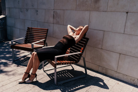 Portrait of a woman on the street. An attractive woman in a black dress is sitting on a bench outside.の写真素材