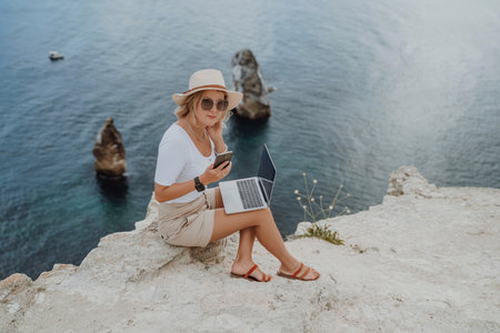 Freelance women sea working on the computer. Good looking middle aged woman typing on a laptop keyboard outdoors with a beautiful sea view. The concept of remote work.の写真素材