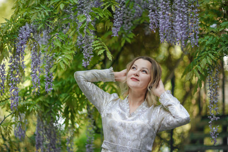 Wisteria woman. Thoughtful happy mature woman surrounded by chinese wisteriaの写真素材