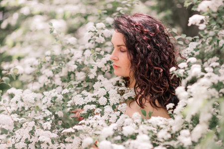 Woman spirea flowers. Portrait of a curly happy woman in a flowering bush with white spirea flowers.の写真素材