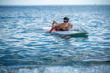 Woman sap sea. Sports girl on a surfboard in the sea on a sunny summer day. In a black bathing suit, he lies on a sap in the sea. Rest on the sea.の写真素材