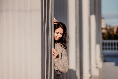 Woman building columns. An athletic woman in her 40s, dressed in a beige sweater and black jeans, poses near the pillars of a building. Walking around the city, tourism.の写真素材