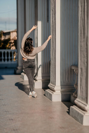 Woman building columns. An athletic woman in her 40s, dressed in a beige sweater and black jeans, poses near the pillars of a building. Walking around the city, tourism.の写真素材