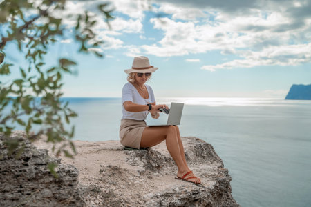Freelance women sea working on the computer. Good looking middle aged woman typing on a laptop keyboard outdoors with a beautiful sea view. The concept of remote work.の写真素材