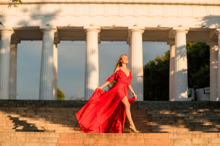 A woman in a long red dress against the backdrop of sunrise, bright golden light of the suns rays. The concept of femininity, harmony.の写真素材