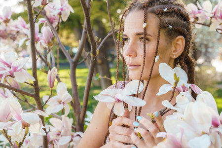 Magnolia flowers. Happy woman enjoys by blooming magnolia tree and sniffs it flowers with closed eyes in spring garden. Portrait.の写真素材