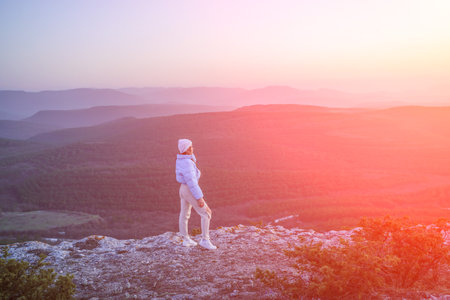Woman tourist on top of sunrise mountain. The girl salutes the sun, wearing a blue jacket, white hat and white jeans. Conceptual design.の写真素材