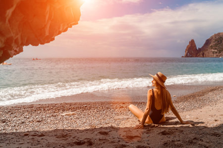 View of a woman in a black swimsuit from a sea cave Attractive woman enjoying the sea air sits on the beach and looks at the sea.の写真素材