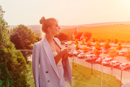A middle-aged woman sits in a street cafe overlooking the mountains at sunset. She is dressed in a...